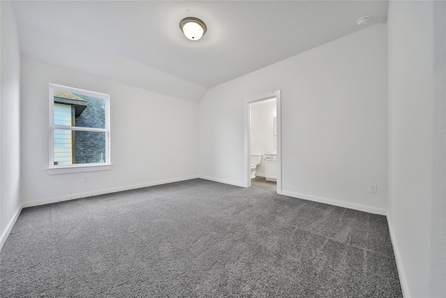 unfurnished bedroom with vaulted ceiling, connected bathroom, and dark carpet