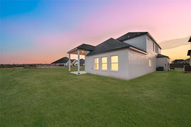 back house at dusk with central AC and a yard