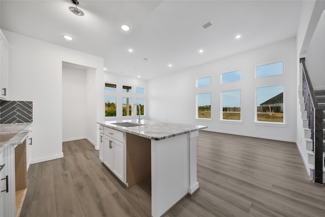 kitchen with decorative backsplash, white cabinetry, a kitchen island with sink, and a healthy amount of sunlight