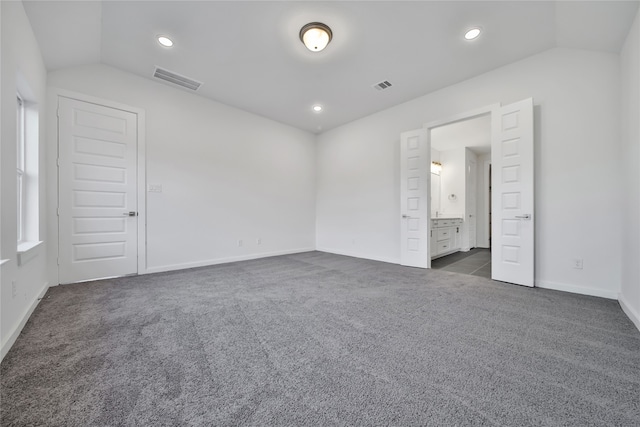 unfurnished bedroom with ensuite bath, dark colored carpet, and vaulted ceiling