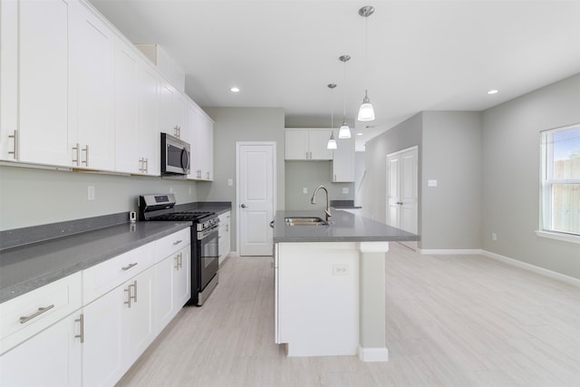 kitchen featuring appliances with stainless steel finishes, decorative light fixtures, white cabinetry, sink, and a center island with sink