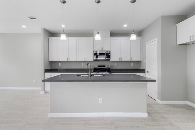 kitchen with appliances with stainless steel finishes, a center island with sink, and white cabinets