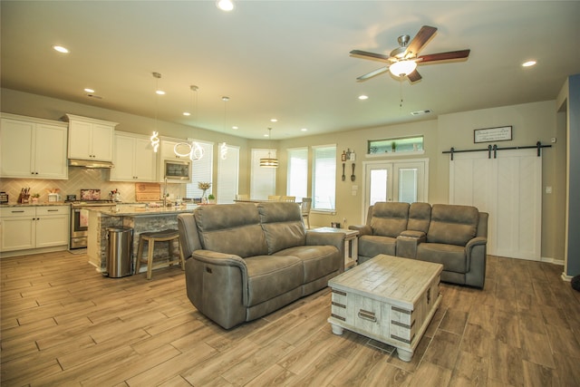 living room featuring ceiling fan, a barn door, and light hardwood / wood-style flooring