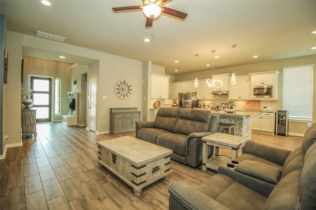 living room with ceiling fan, beverage cooler, and light hardwood / wood-style flooring