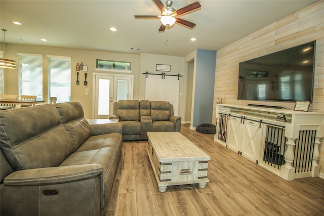 living room with light wood-type flooring, ceiling fan, and a barn door