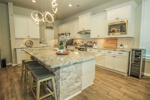 kitchen featuring a kitchen island, beverage cooler, white cabinetry, appliances with stainless steel finishes, and light hardwood / wood-style floors