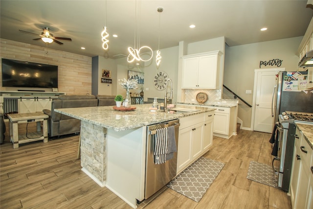 kitchen with stainless steel appliances, white cabinets, sink, a center island with sink, and decorative light fixtures