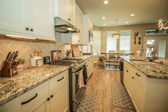 kitchen featuring light wood-type flooring, stainless steel appliances, white cabinets, sink, and decorative light fixtures