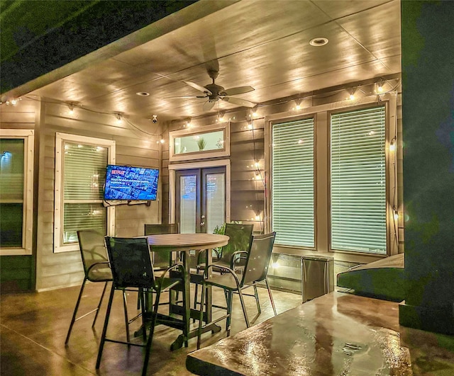 dining room featuring ceiling fan, wood walls, french doors, and concrete flooring