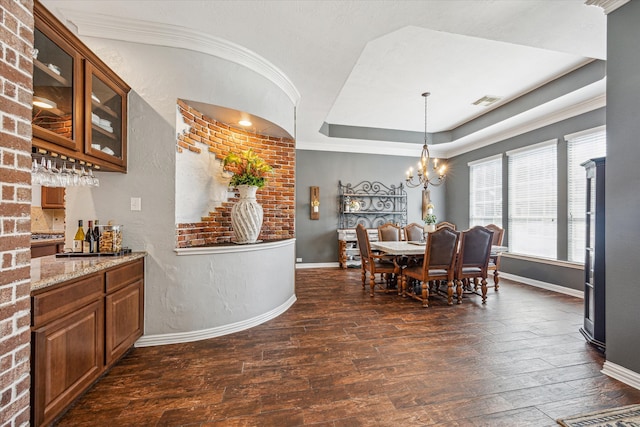 dining room featuring dark wood-type flooring, brick wall, a tray ceiling, an inviting chandelier, and crown molding