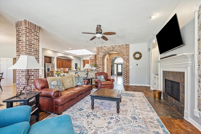 living room with ceiling fan, dark hardwood / wood-style flooring, a tiled fireplace, and brick wall