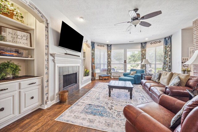 living room featuring built in features, a fireplace, a textured ceiling, dark wood-type flooring, and ceiling fan