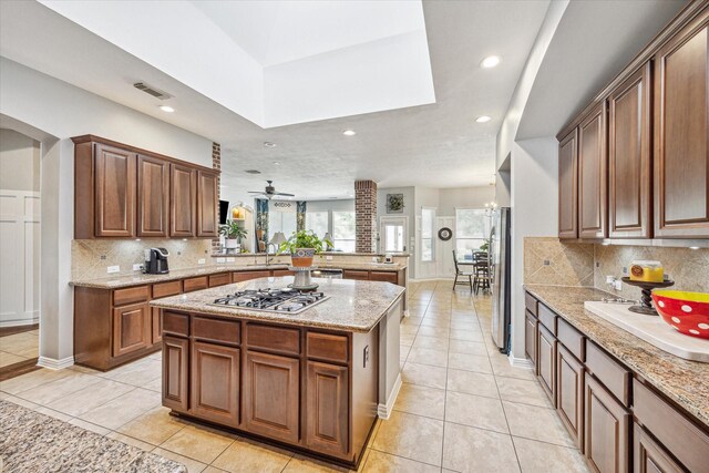 kitchen with appliances with stainless steel finishes, tasteful backsplash, light tile patterned floors, a center island, and ceiling fan