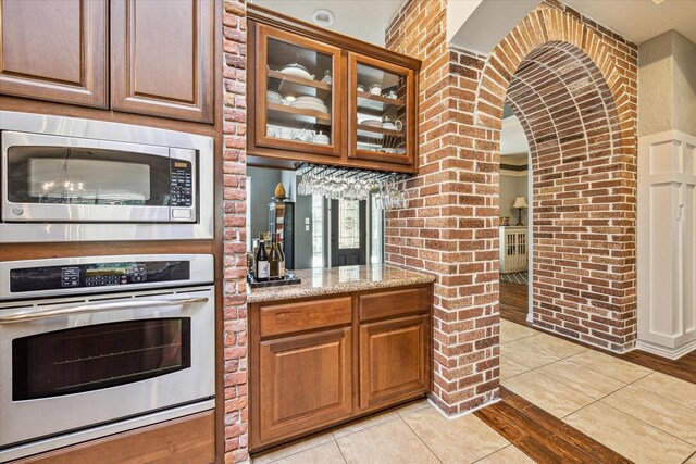 kitchen featuring stainless steel appliances, light tile patterned flooring, brick wall, and light stone counters