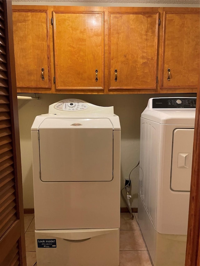clothes washing area with washer and clothes dryer, light tile patterned flooring, and cabinet space