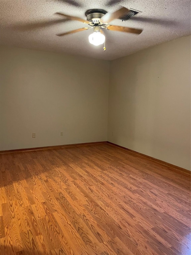 unfurnished room with a textured ceiling, wood finished floors, ceiling fan, and visible vents