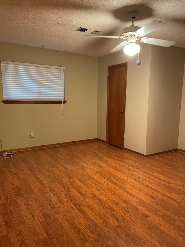 spare room featuring light wood-style floors, ceiling fan, baseboards, and a textured ceiling