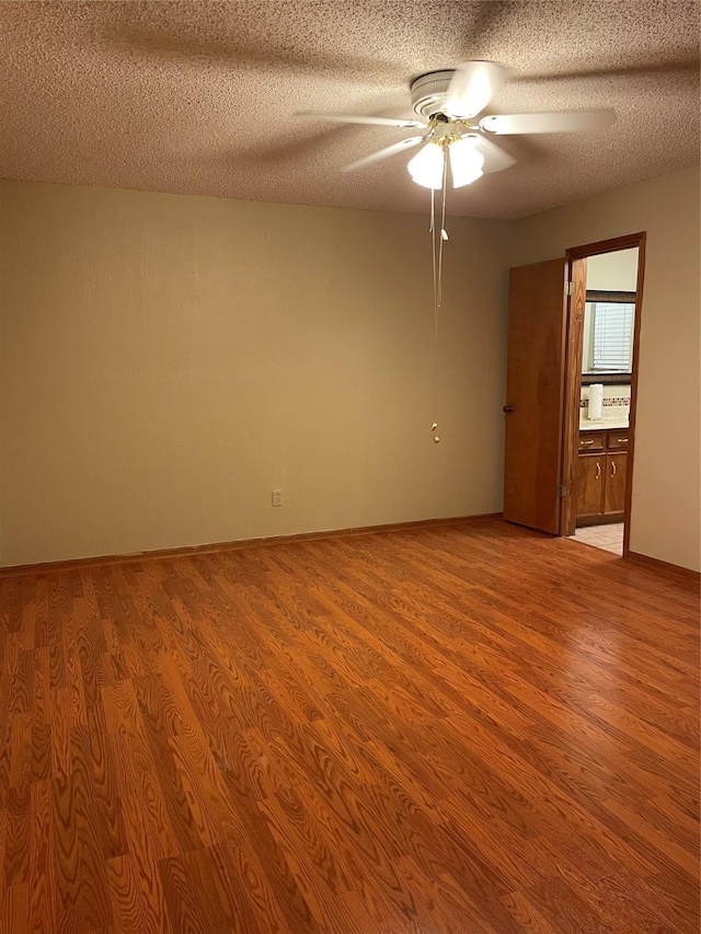 spare room featuring light wood finished floors, a textured ceiling, baseboards, and ceiling fan