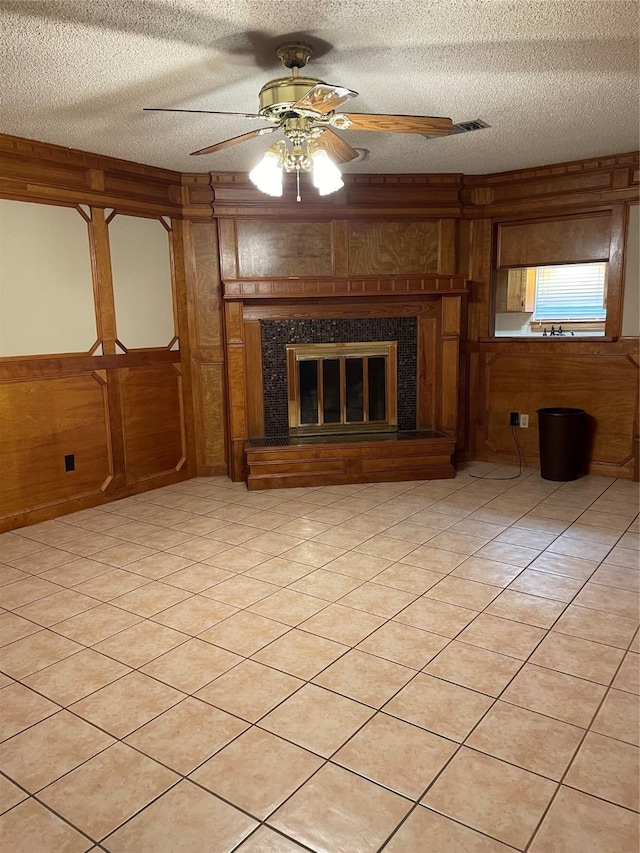 unfurnished living room featuring a textured ceiling, wood walls, ceiling fan, and a fireplace