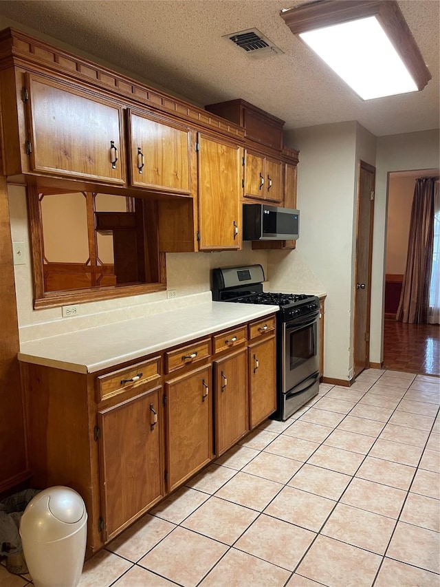kitchen featuring visible vents, light countertops, stainless steel range with gas cooktop, brown cabinets, and light tile patterned flooring