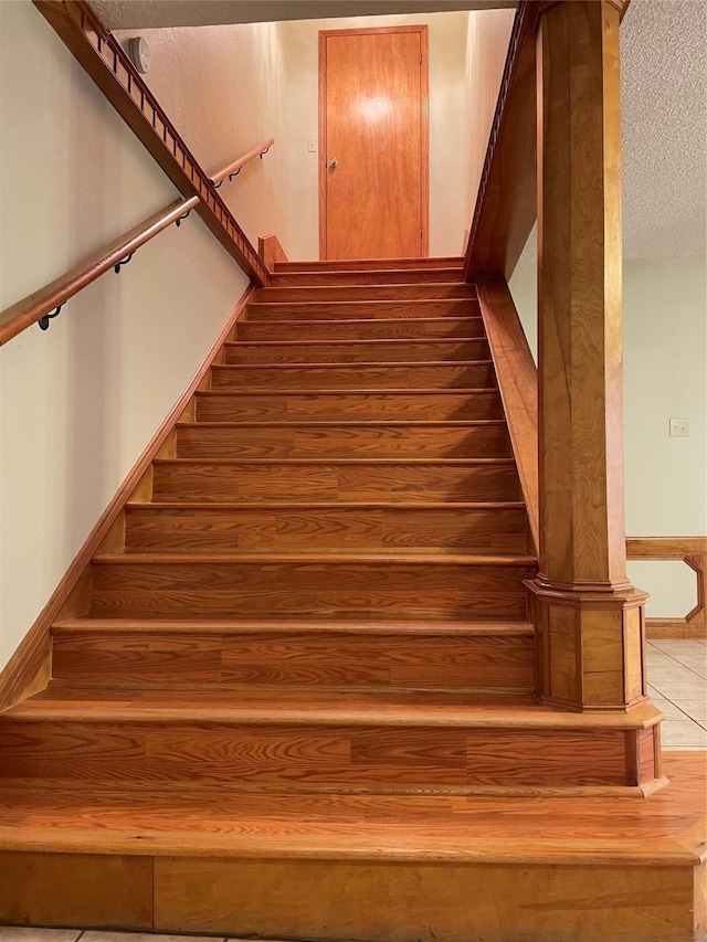 staircase with wood finished floors and a textured ceiling