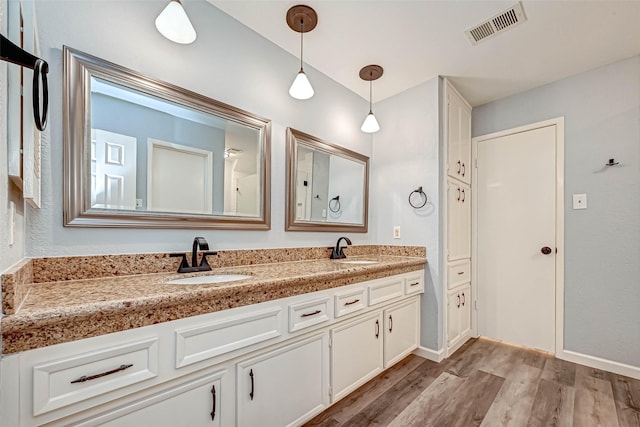 bathroom with a sink, visible vents, wood finished floors, and double vanity