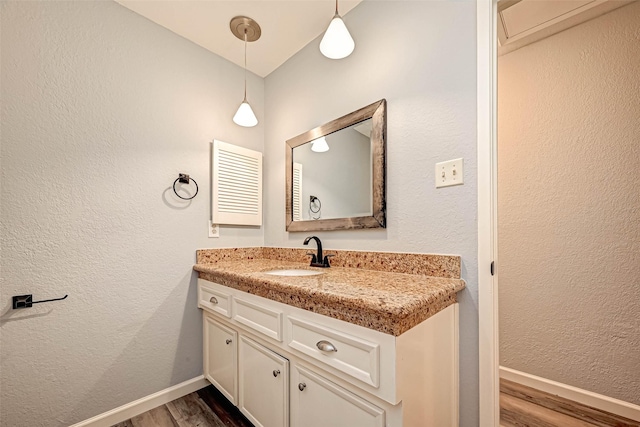 bathroom featuring a textured wall, vanity, baseboards, and wood finished floors