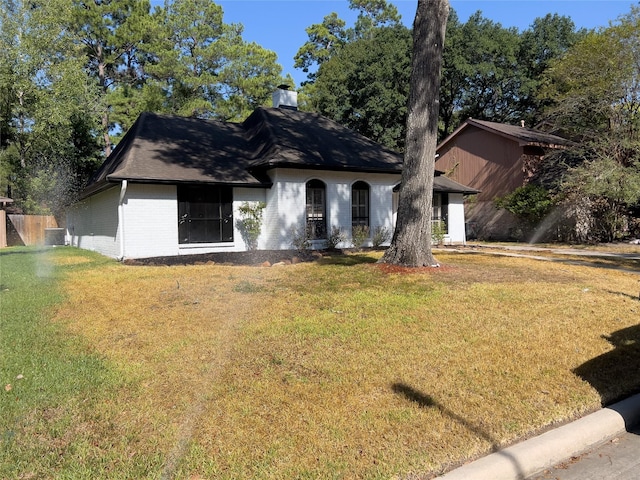 view of front of property with a front yard, brick siding, central AC, and a chimney