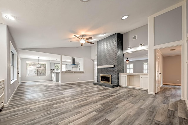 unfurnished living room featuring visible vents, a ceiling fan, wood finished floors, a brick fireplace, and vaulted ceiling