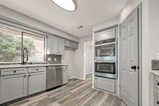 kitchen featuring backsplash, sink, gray cabinets, light hardwood / wood-style floors, and stainless steel appliances