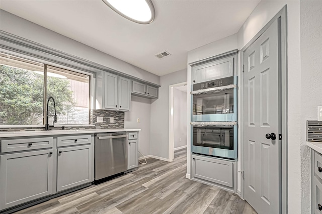 kitchen featuring visible vents, gray cabinetry, light wood-type flooring, decorative backsplash, and appliances with stainless steel finishes