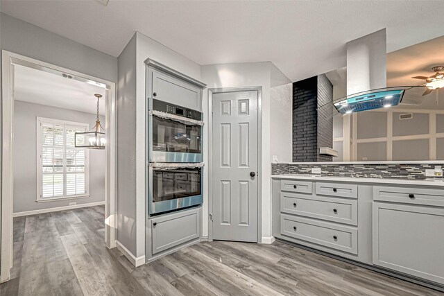 kitchen featuring tasteful backsplash, light hardwood / wood-style floors, double oven, and island exhaust hood