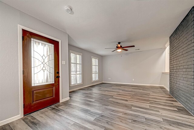 foyer entrance with ceiling fan, light hardwood / wood-style flooring, and brick wall