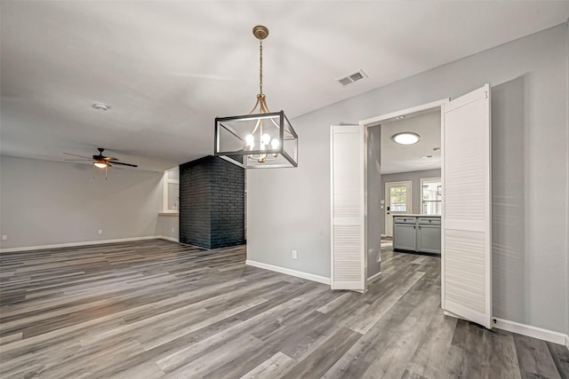 unfurnished dining area featuring visible vents, baseboards, wood finished floors, and ceiling fan with notable chandelier