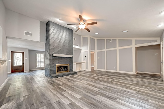 unfurnished living room with visible vents, wood finished floors, ceiling fan, and a fireplace