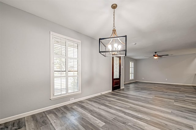 interior space featuring plenty of natural light, ceiling fan with notable chandelier, baseboards, and wood finished floors