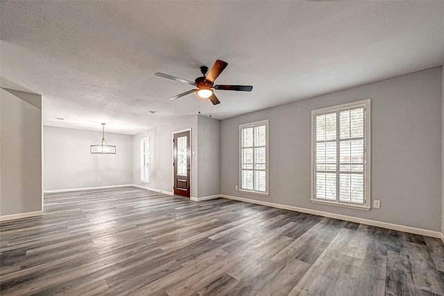 unfurnished living room featuring ceiling fan with notable chandelier, dark wood-style floors, and baseboards
