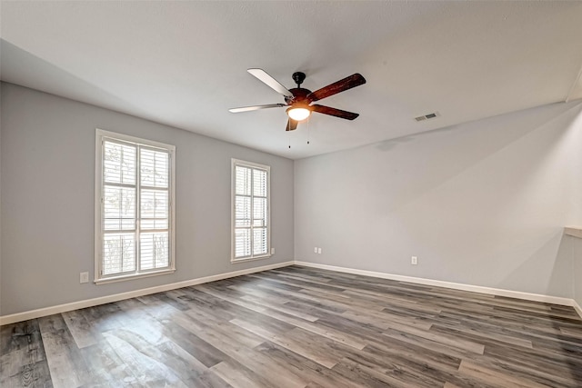 spare room featuring ceiling fan, visible vents, baseboards, and wood finished floors