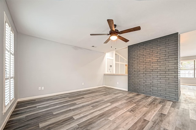empty room featuring visible vents, a ceiling fan, wood finished floors, brick wall, and baseboards
