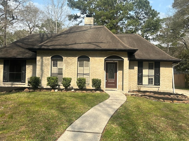 view of front of property with brick siding, a chimney, a front yard, and a shingled roof