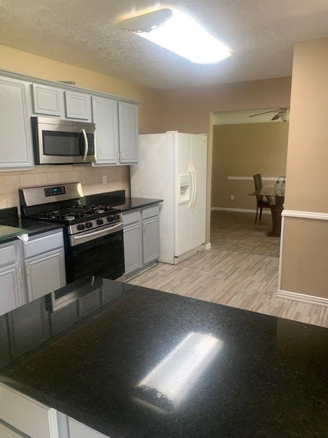 kitchen featuring ceiling fan, light hardwood / wood-style flooring, backsplash, white cabinets, and stainless steel appliances