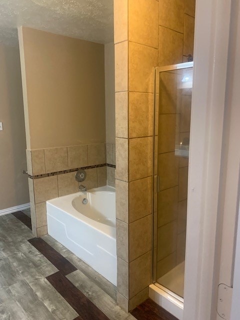 bathroom with a textured ceiling, shower with separate bathtub, and hardwood / wood-style flooring