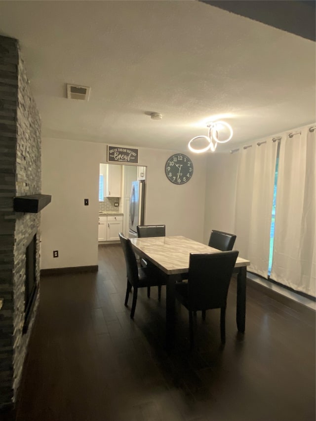 dining area with dark wood-type flooring and a stone fireplace