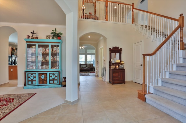 tiled entrance foyer with ceiling fan, crown molding, and a towering ceiling