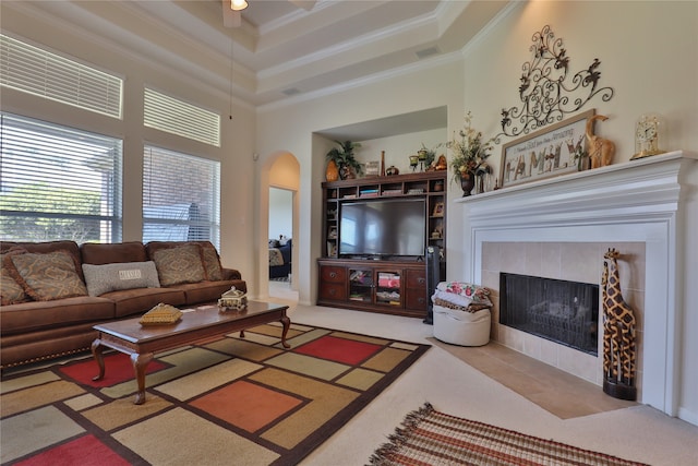 carpeted living room featuring a towering ceiling, ceiling fan, a tiled fireplace, and ornamental molding