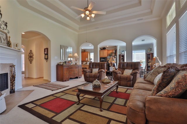 living room with ornamental molding, a tile fireplace, a tray ceiling, ceiling fan, and a towering ceiling