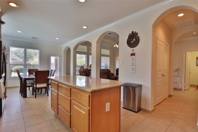 kitchen featuring crown molding, light stone countertops, a center island, ceiling fan, and light tile patterned flooring