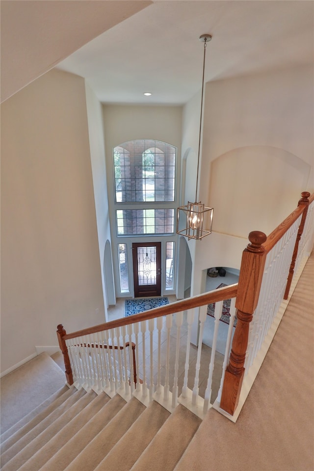 stairs with a towering ceiling, carpet flooring, and a notable chandelier