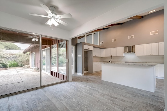 kitchen with light wood-type flooring, visible vents, white cabinetry, and wall chimney range hood