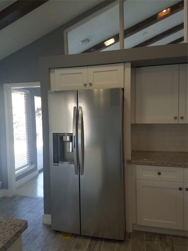 kitchen featuring stainless steel refrigerator with ice dispenser, visible vents, wood tiled floor, white cabinets, and vaulted ceiling